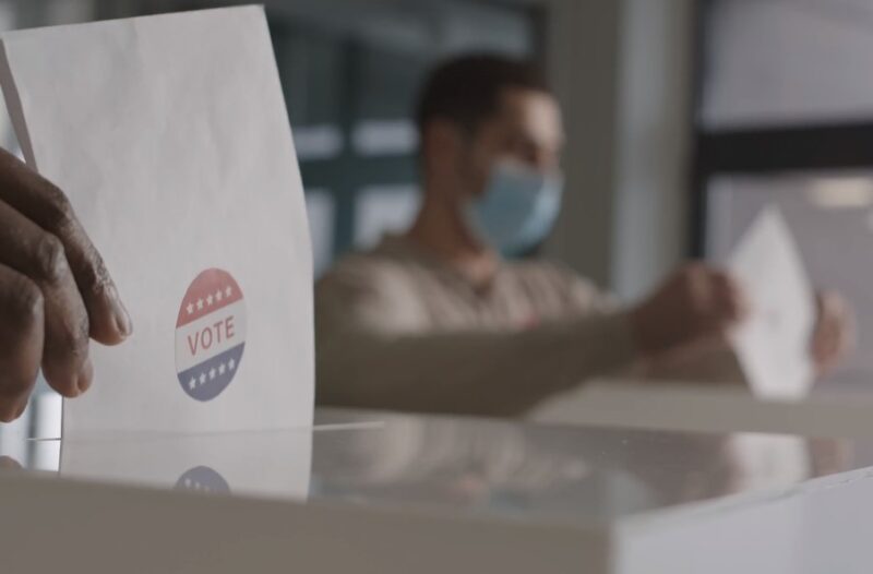 people putting voting paper in a box